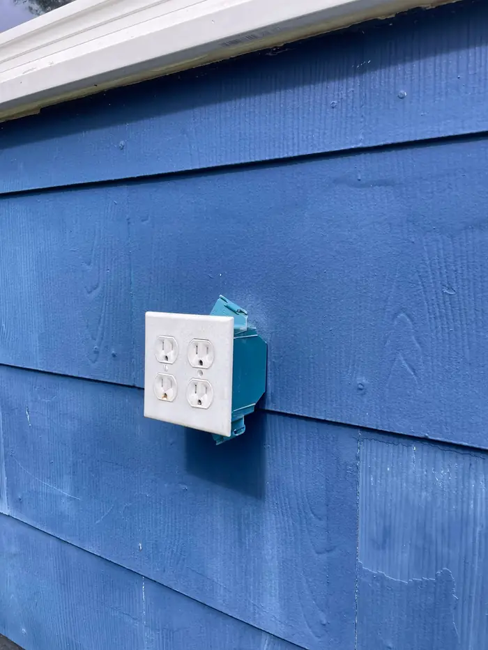 Exterior receptacle being set into its box on wood siding