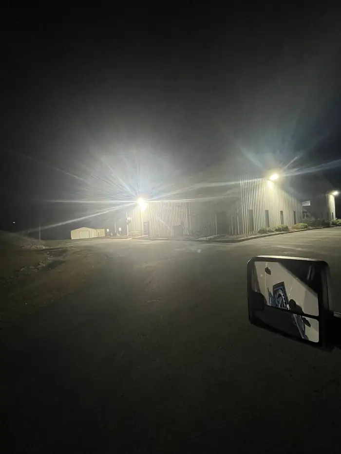 Pole lights lit over a parking lot and the side of a commercial building at night