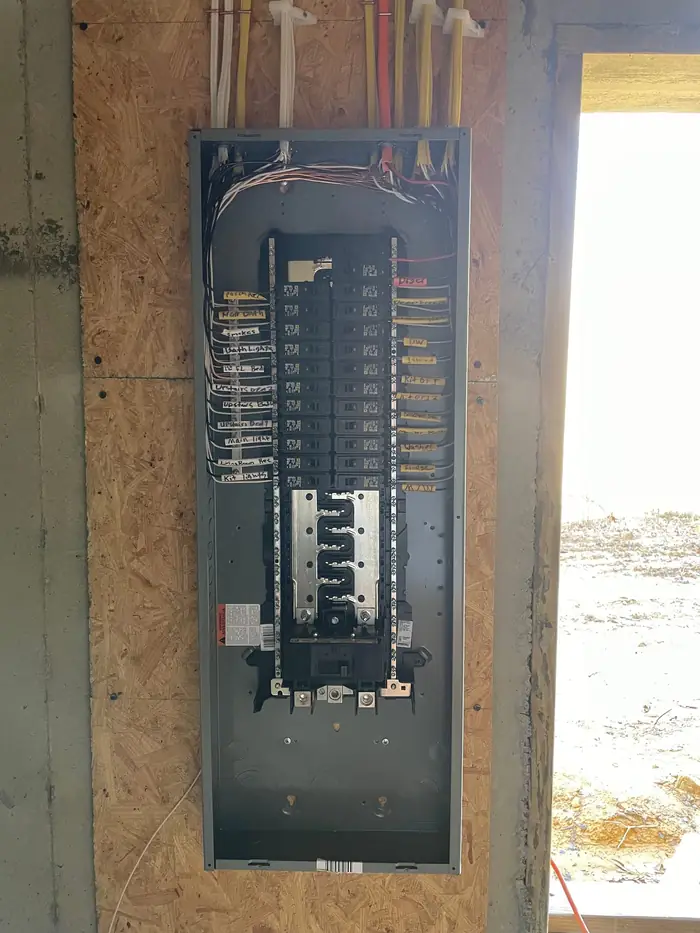 New breaker panel set into an open stud bay with the cover off, every circuit landed and tagged