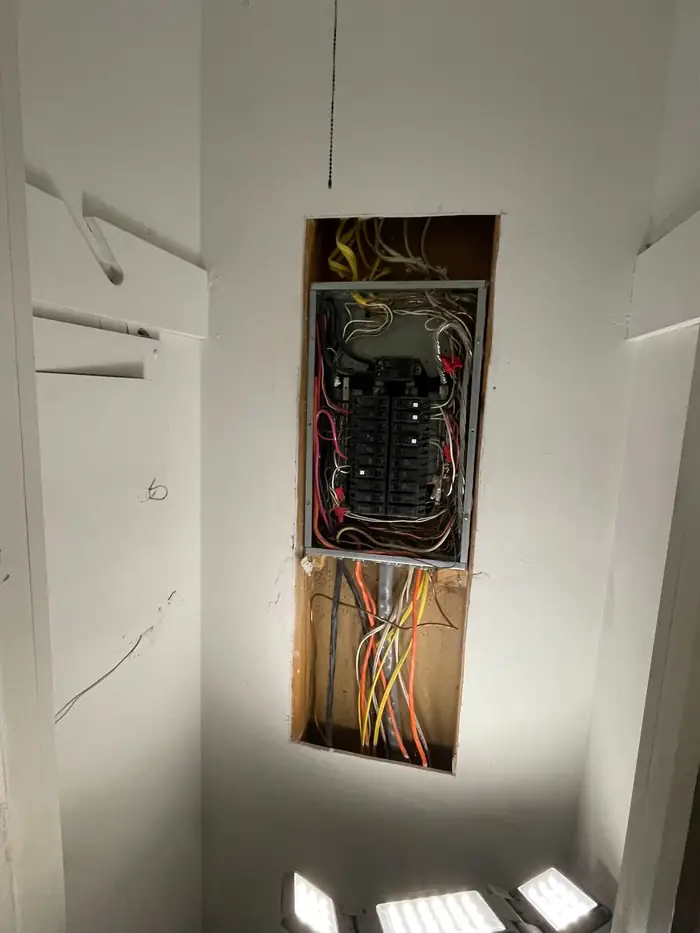 Breaker panel in an opened interior wall with the cover off and conductors run into the cabinet
