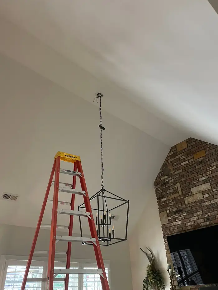 Lantern pendant fixture being hung from a vaulted ceiling with a ladder in place